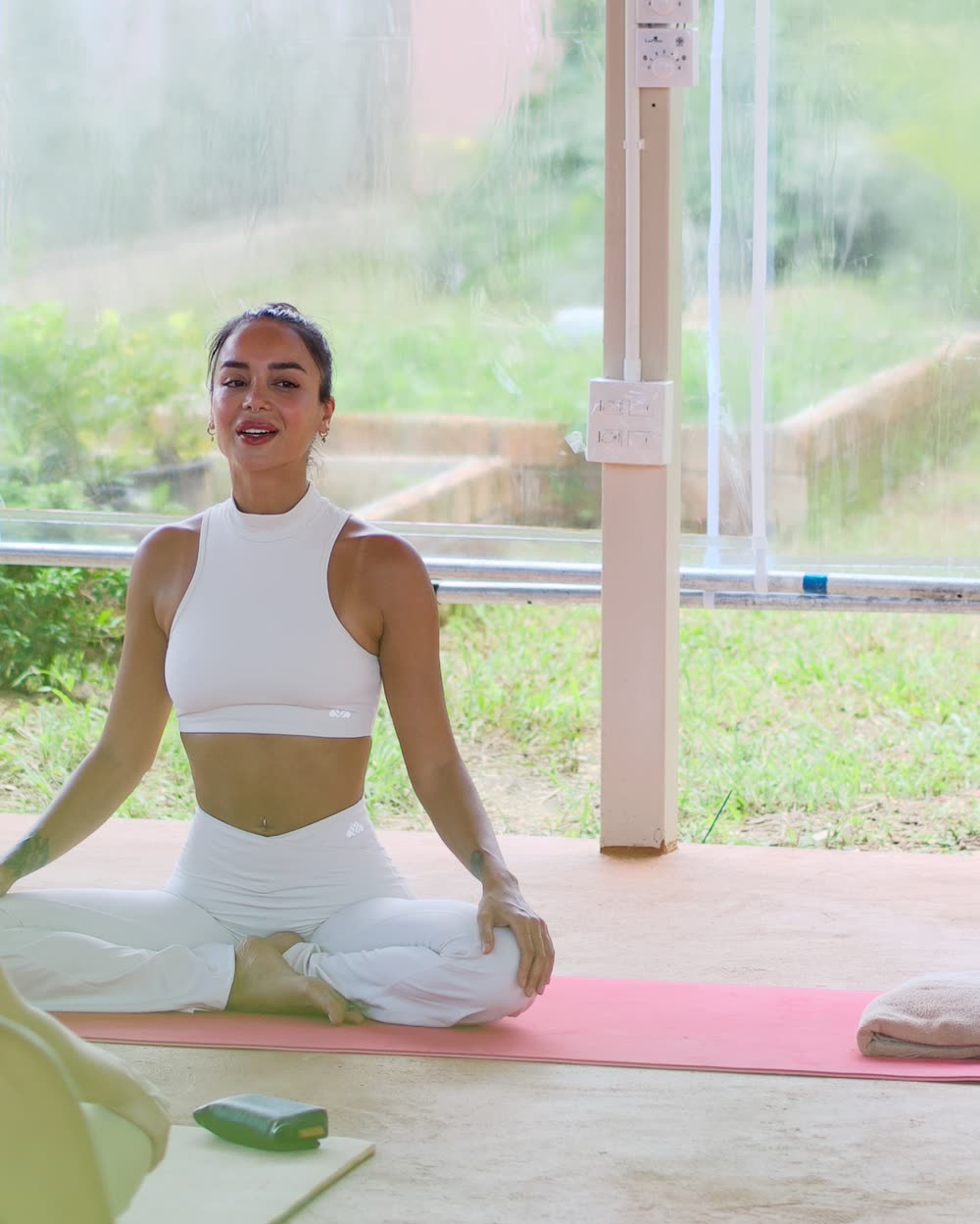 A yoga teacher seated cross-legged on a mat, leading the breath
