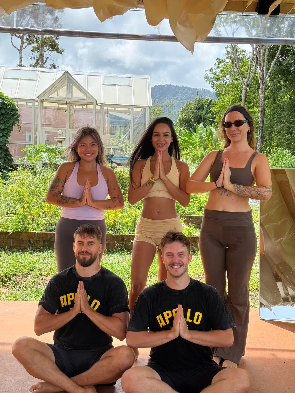Five practitioners with hands at the heart at the close of a class, the hills behind the farm