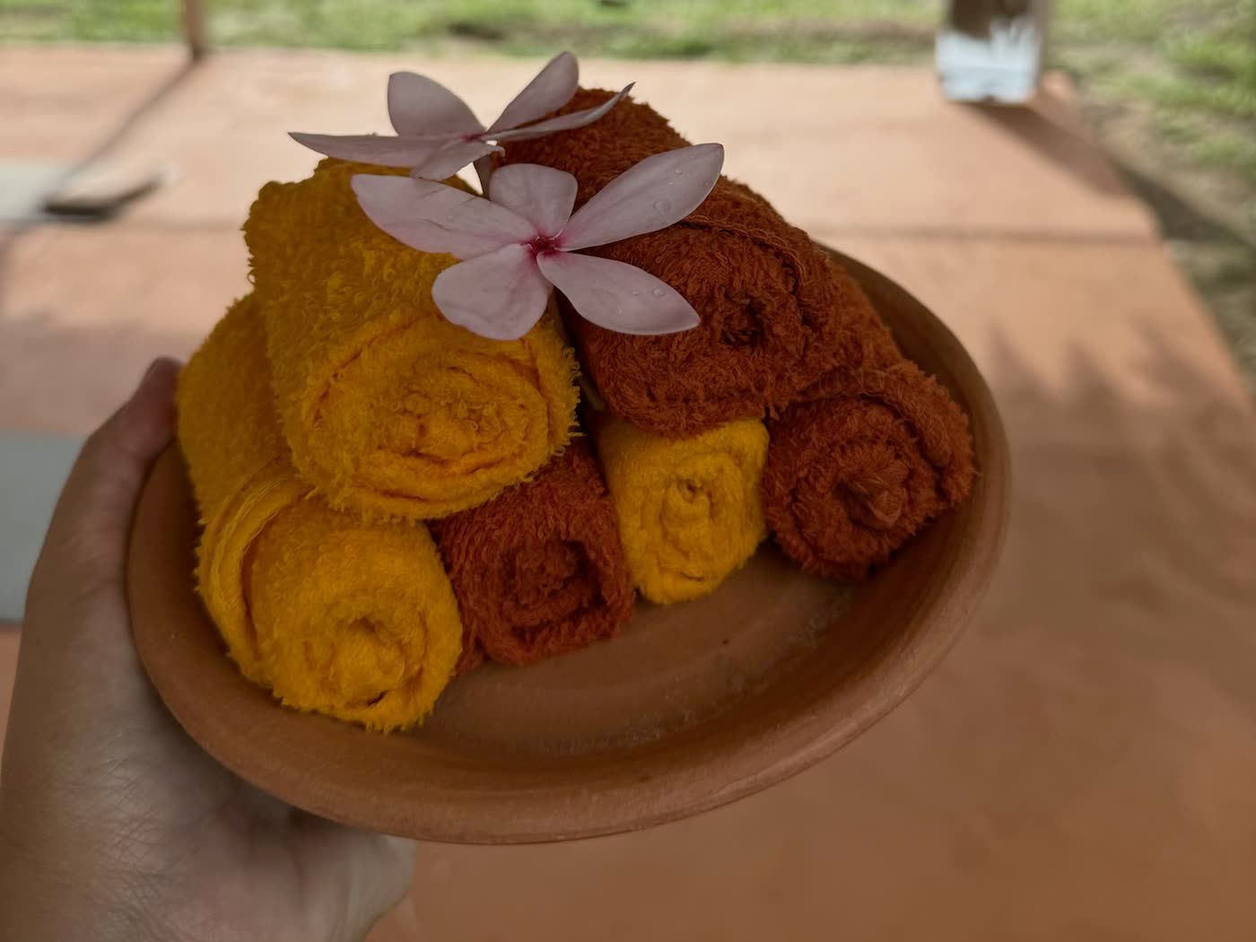 Rolled cotton towels on a terracotta plate with a frangipani flower
